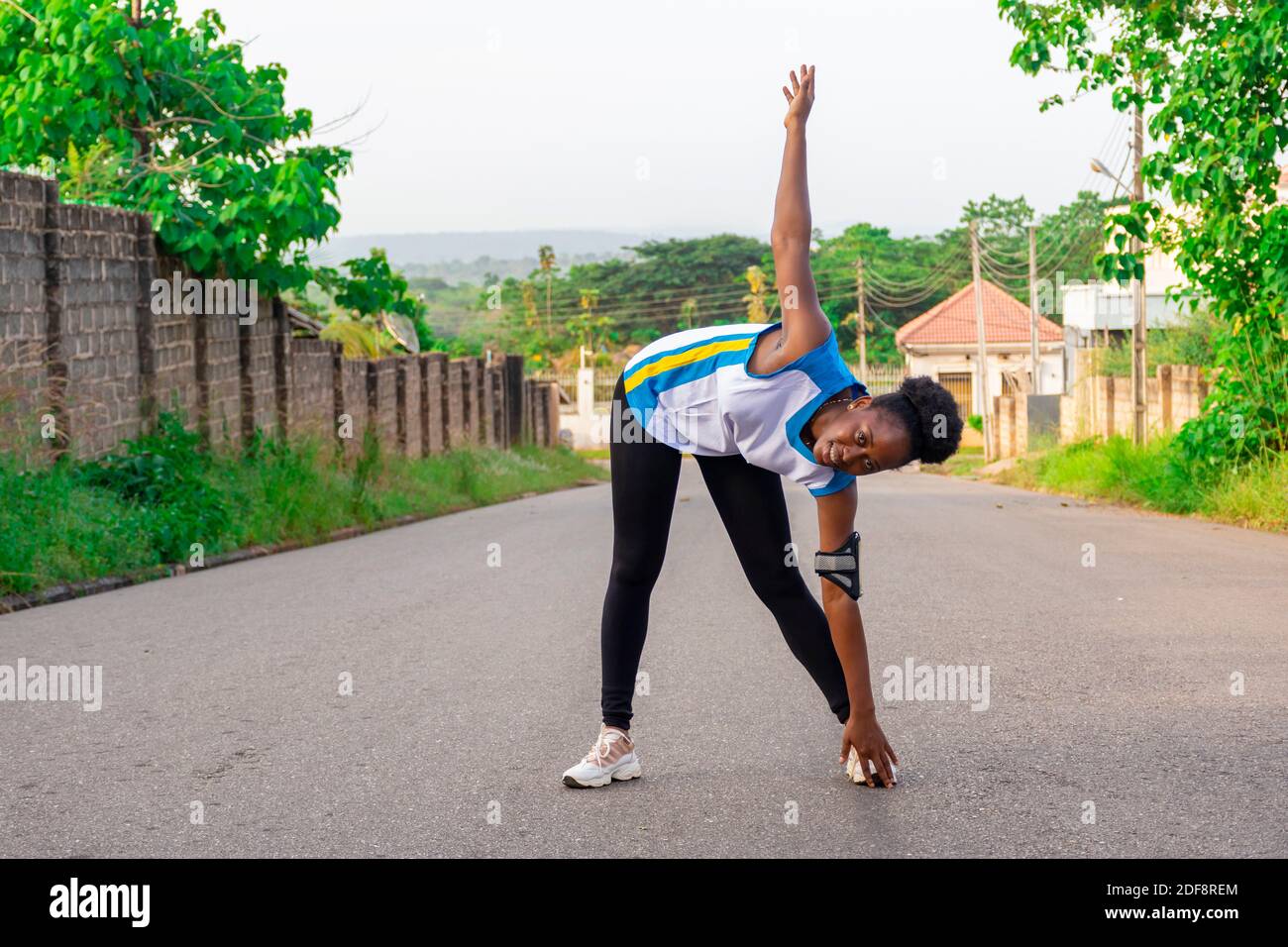 bella donna africana fare esercizio all'aperto sulla strada, stretching e toccare le dita dei piedi Foto Stock