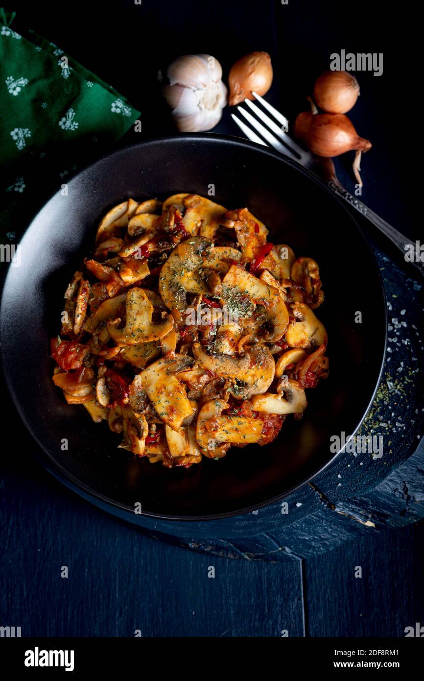 Funghi cotti con erbe e spezie in piastra nera. Funghi saltati. Foto Stock