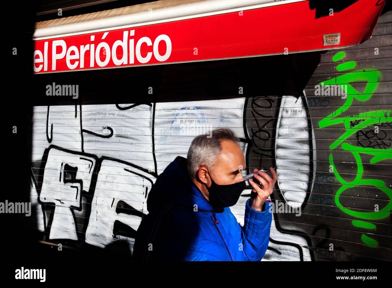 Uomo che parla al telefono indossando una maschera a piedi davanti a un chiosco chiuso, Barcellona, Spagna. Foto Stock