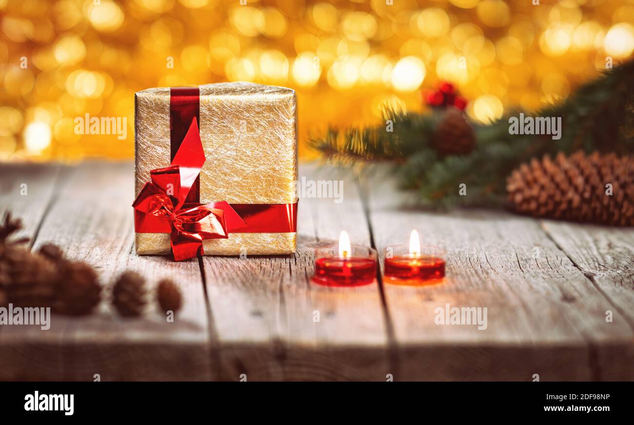 Scatola regalo d'oro e ramo di pino con coni con candele su tavolo di legno. Sfondo bokeh luci gialle. Vacanze di Natale e Capodanno a tema decoratio Foto Stock