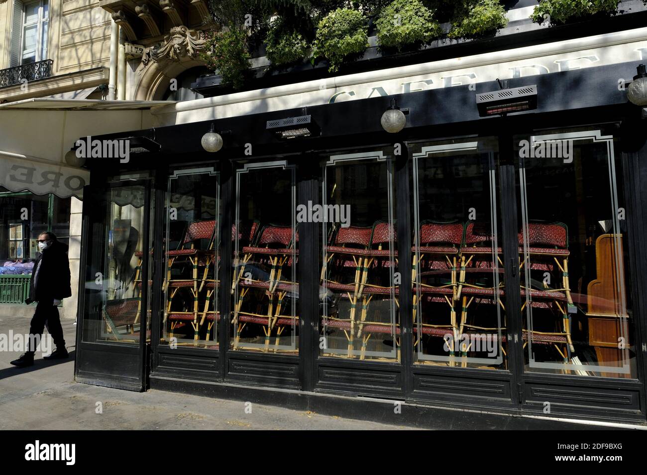 Un uomo che indossa una maschera facciale guarda il caffè Les Deux Magots chiuso nel quartiere Saint-Germain-des-Prés di Parigi, mentre i caffè e i ristoranti sono chiusi in mezzo al COVID-19 focolaio, Causato dal novo coronavirus... dopo l'annuncio da parte del presidente francese Emmanuel Macron delle severe regole di isolamento domestico dei francesi a causa di un focolaio di pandemia di coronavirus (COVID-19) il 18 marzo 2020 a Parigi, Francia, i francesi dovranno rimanere a casa, La Francia ha chiuso tutte le scuole, i teatri, i cinema e una serie di negozi, con solo quelli che vendono cibo e altri articoli essenziali autorizzati a rimanere aperti Foto Stock