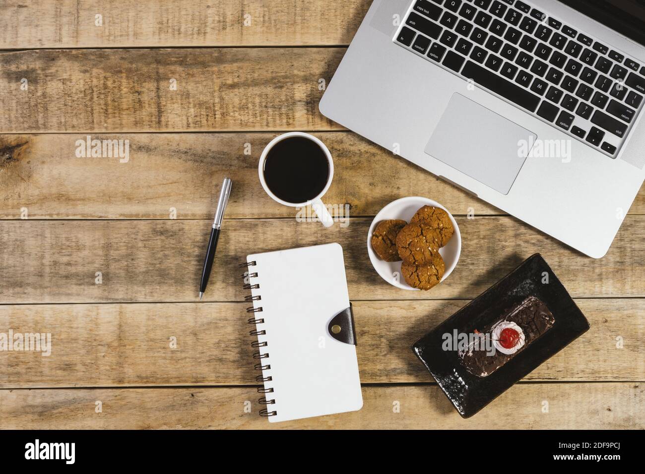 Laptop, diario, torta di butterscotch e tazza di caffè su legno rustico. Disposizione piatta. Foto Stock