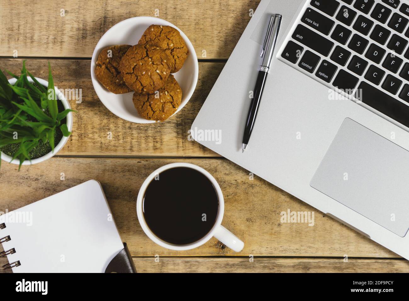Computer portatile, agenda, biscotti e tazza di caffè su legno rustico. Disposizione piatta. Foto Stock