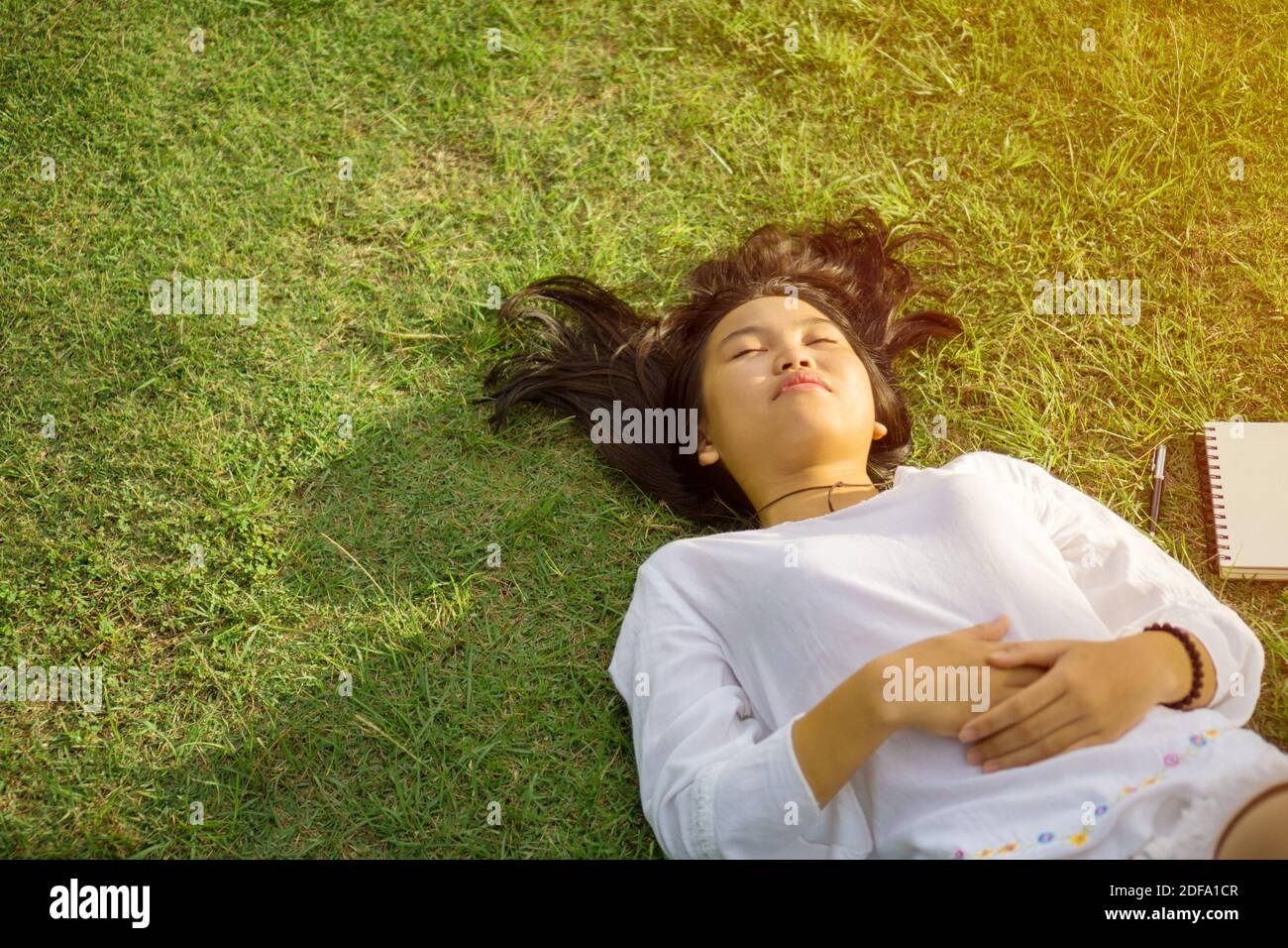 Giovane ragazza asiatica sdraiata sull'erba nel parco e godendo il momento della pace. Foto Stock