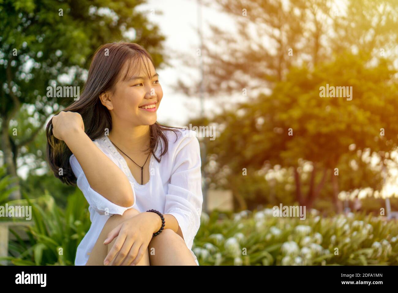 Felice sorridente giovane ragazza asiatica teenage seduta e che si capovolge i capelli. Foto Stock