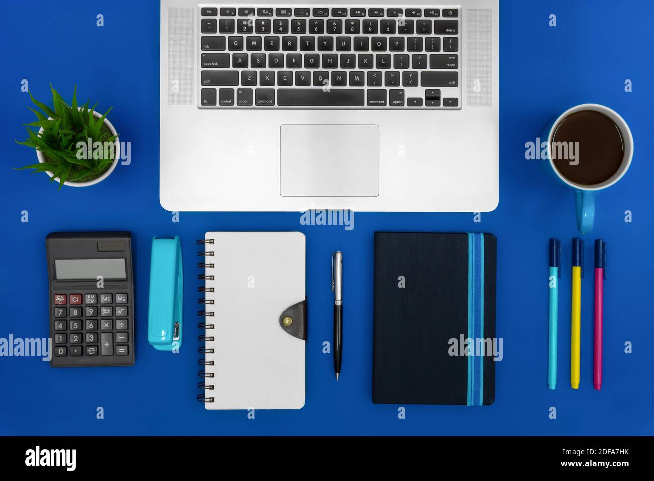 Scrivania da ufficio. Computer portatile, notebook, calcolatrice e caffè su sfondo blu. Concetto aziendale. Foto Stock