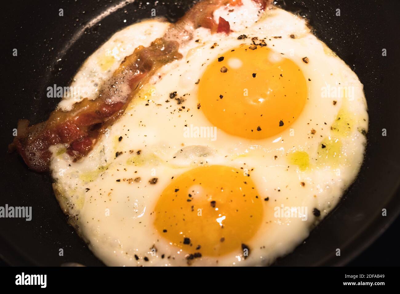 Cucina per la colazione soleggiato con uova e pancetta in una padella Foto Stock