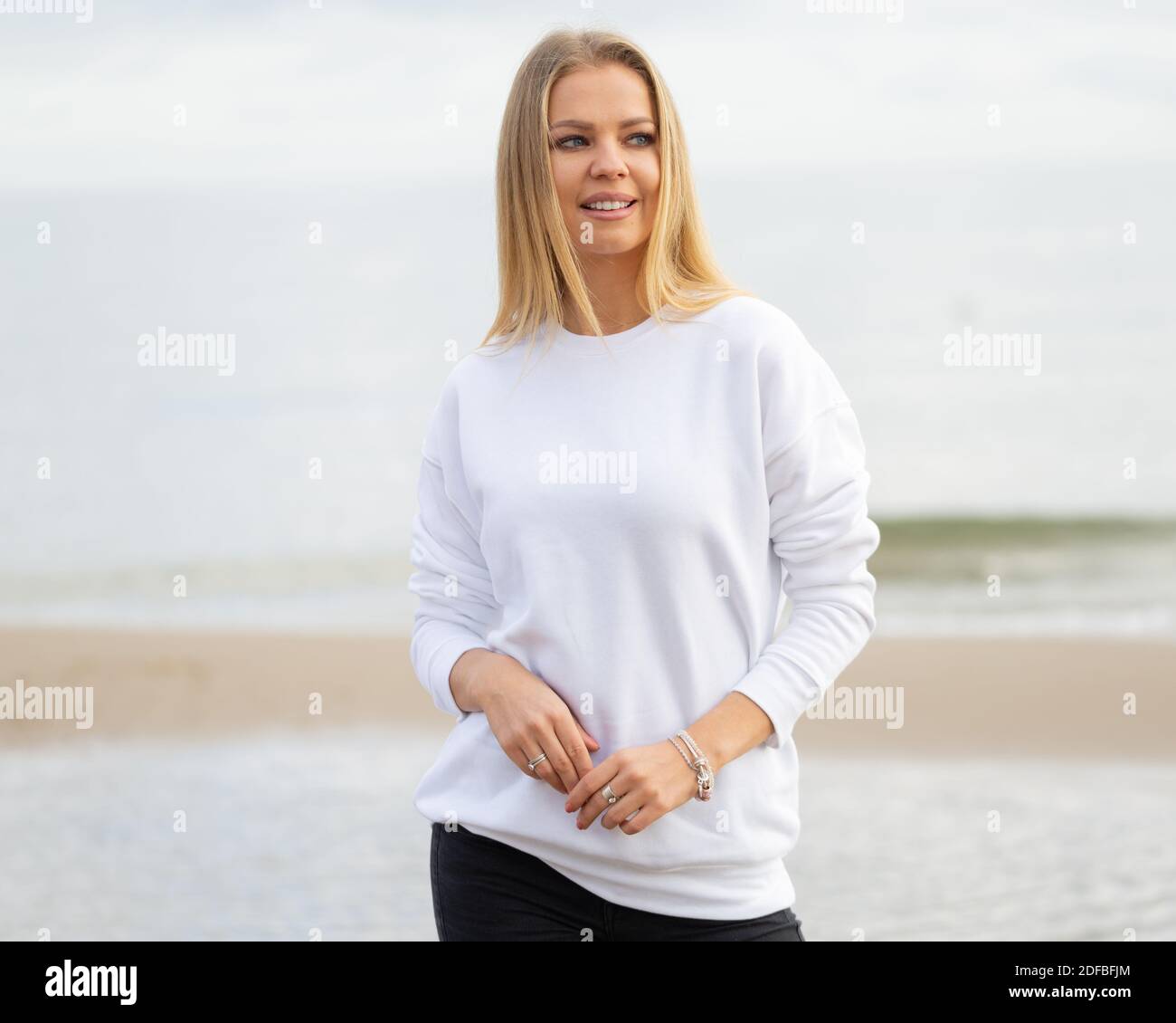 La giovane donna indossa una blusa bianca in estate o in autunno. Donna bionda si trova di fronte alla macchina fotografica sulla spiaggia, all'aperto. Moda mockup con spazio di copia. Foto Stock