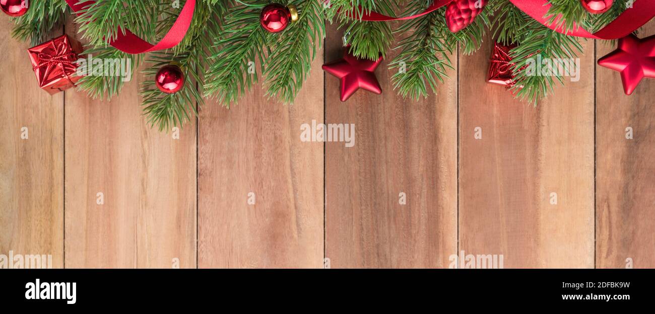 Foglie verdi dell'albero di Natale con ornamenti rossi luminosi su sfondo di legno, banner di disegno di bordo Foto Stock