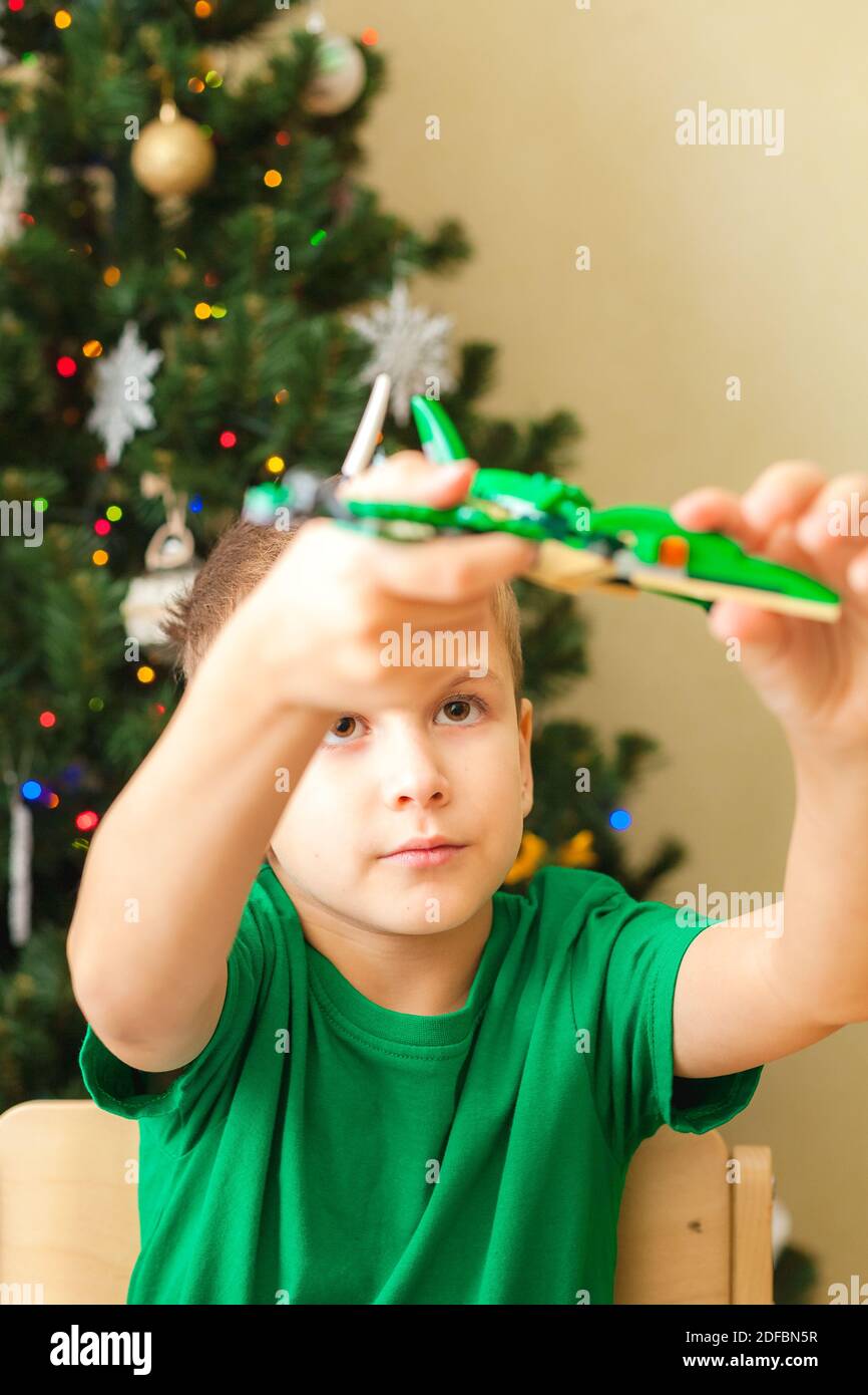 Gioco di ragazzo con pterodattile fatto da blocchi di plastica. Albero di Natale in background. Mettere a fuoco sul viso dei bambini Foto Stock
