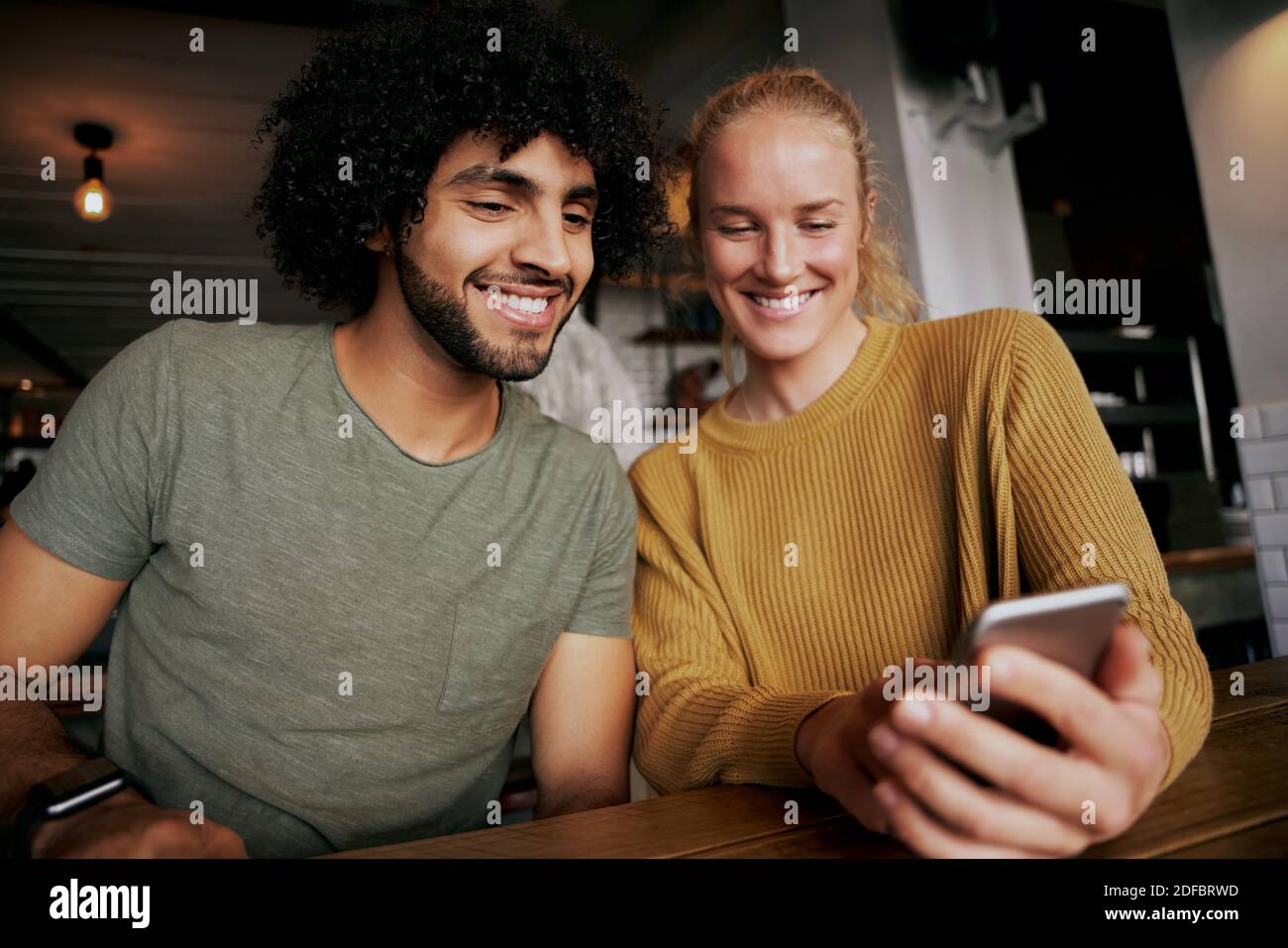 Ritratto di una coppia felice con lo smartphone e sorridente mentre si è seduti e rilassarsi nella caffetteria Foto Stock