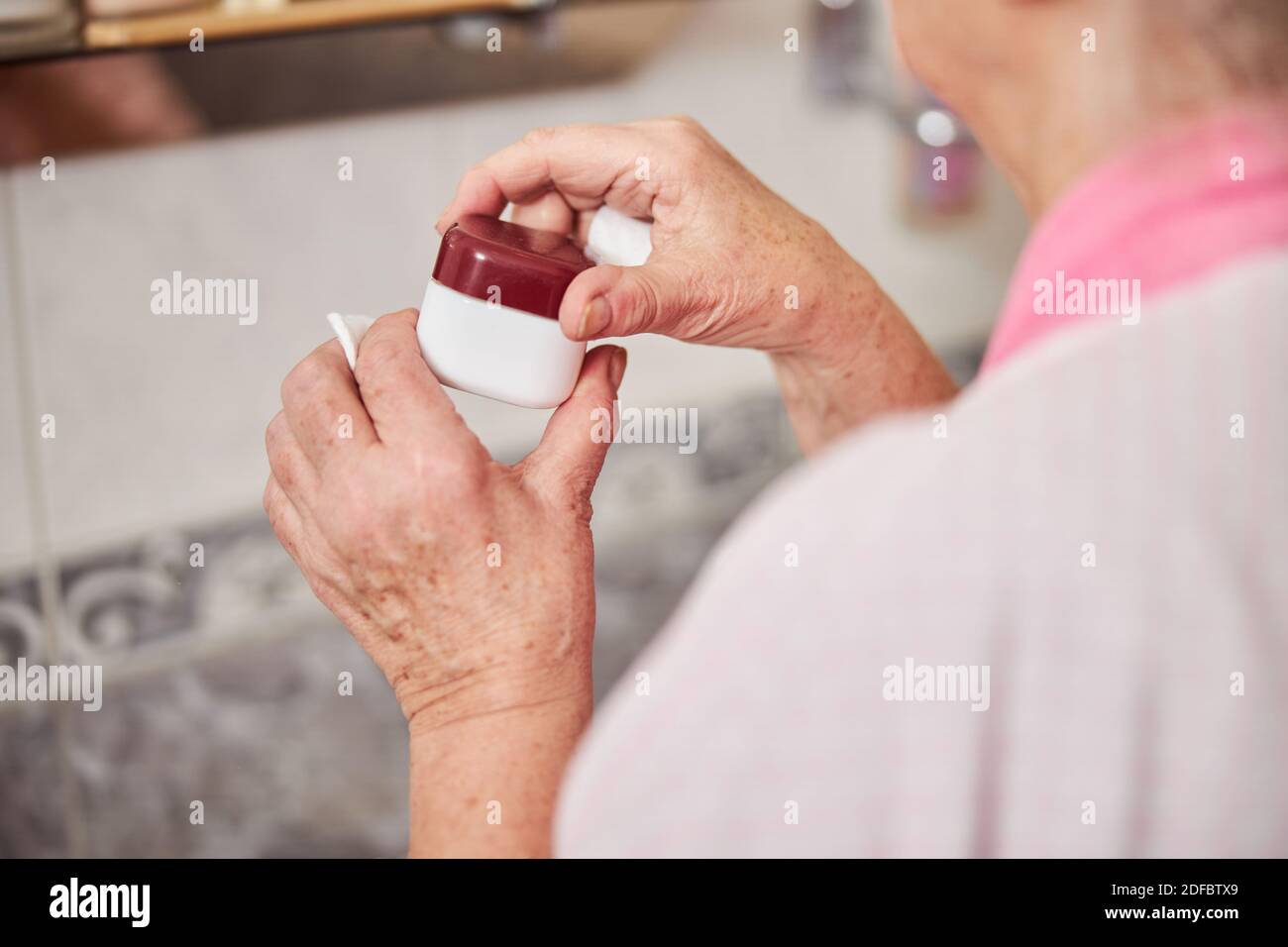 Vecchie mani femminili che tengono il vaso di crema cosmetica Foto Stock