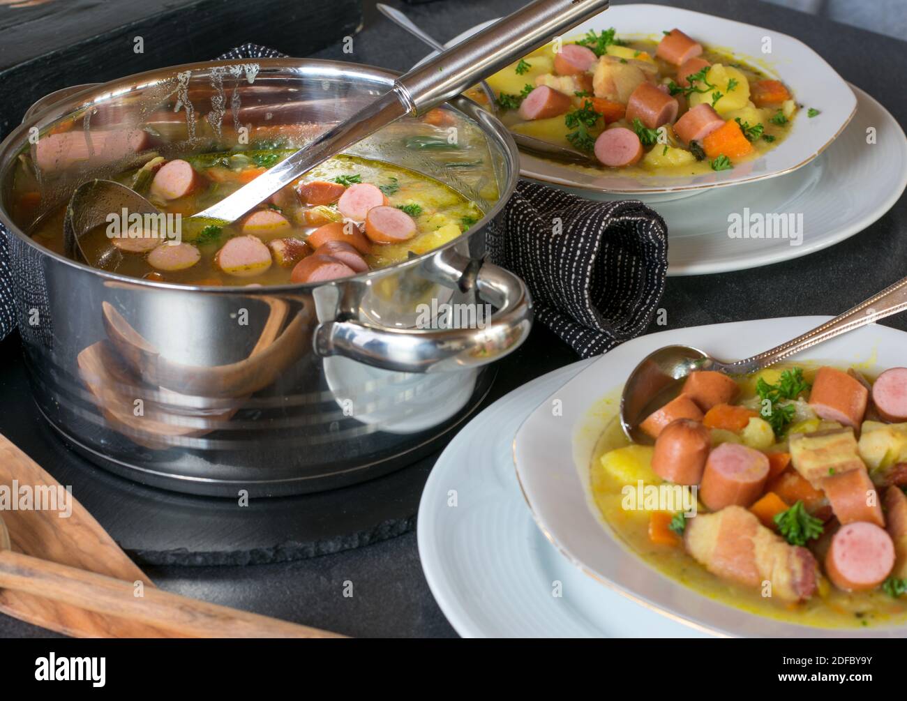 Zuppa di patate tedesca con cane caldo e verdure servite su un tavolo con pentola, mestolo e piatto Foto Stock