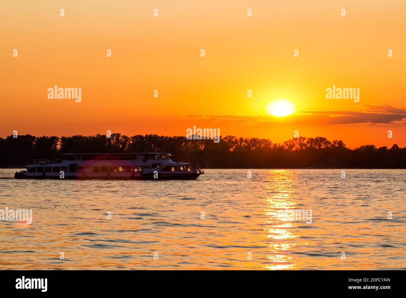 Una piccola escursione in barca fluviale galleggia sul fiume contro il sfondo di un tramonto pittoresco Foto Stock