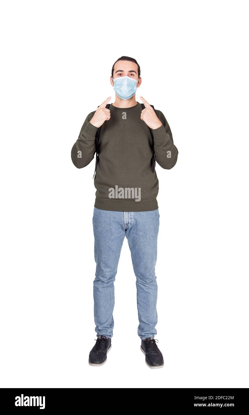 Ritratto a lunghezza intera di un giovane cauto che punta le dita di indice alla sua maschera facciale come avvertimento per la protezione contro il coronavirus, isolato su bianco. C Foto Stock