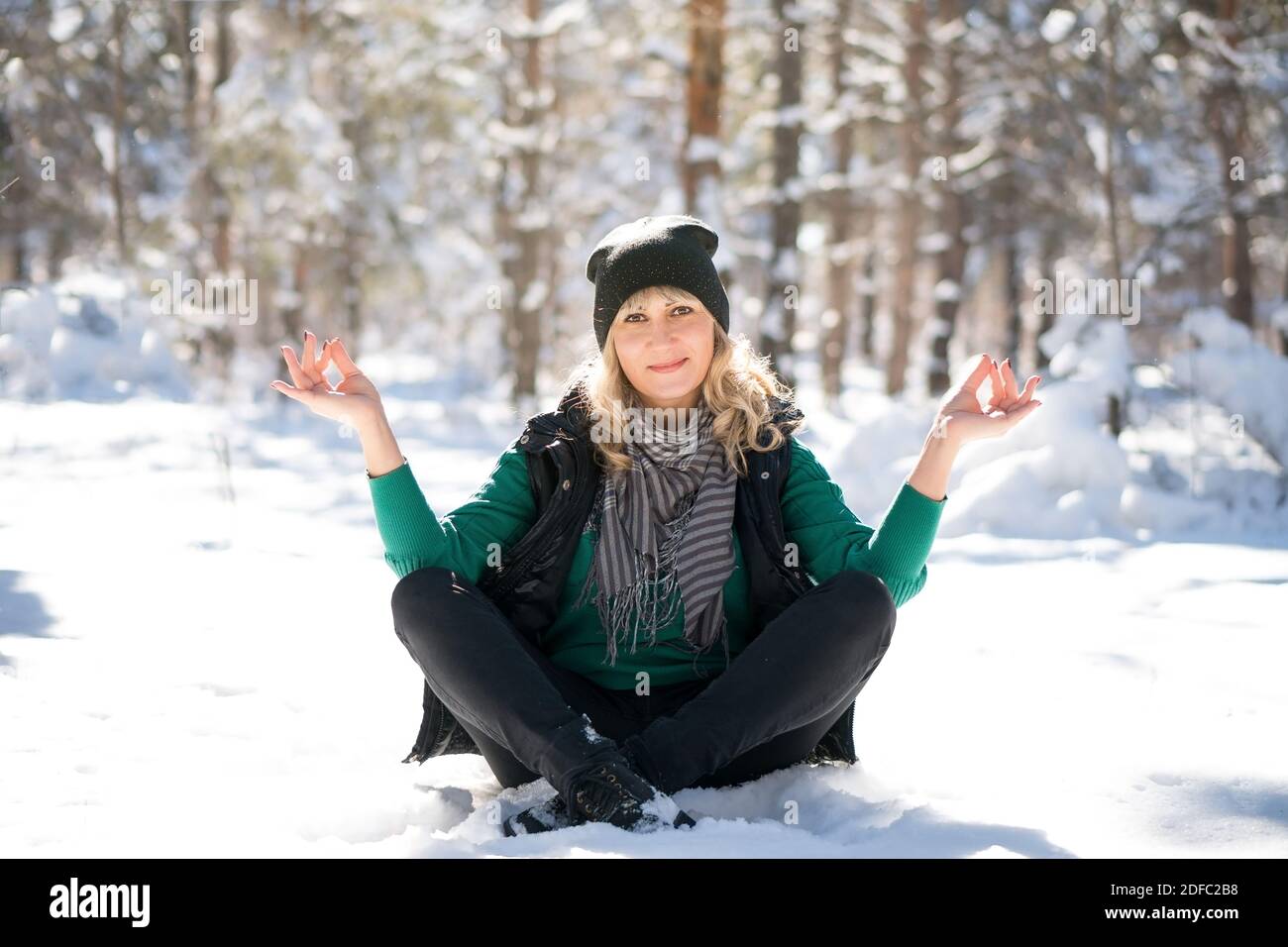 Bella donna si siede in posizione yoga in foresta ghiacciata. Lady meditando e contemplando il paesaggio. Giorno invernale in vacanza, all'aperto. Foto Stock