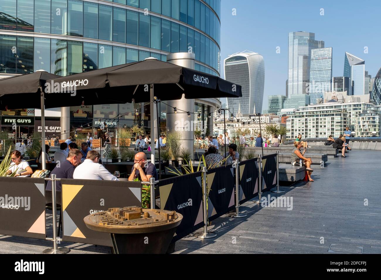 La gente mangia all'aperto al ristorante Gaucho (Tower Bridge) con la City of London nel Backround, London Bridge City Area, Londra, Regno Unito. Foto Stock