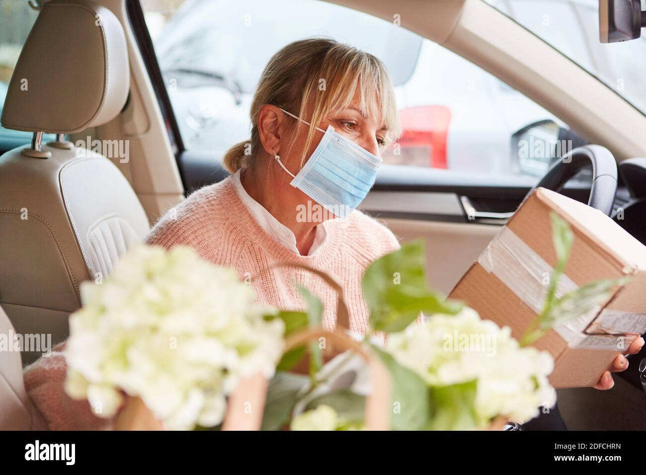 Donna con maschera facciale in auto controlli interni pacchetto dopo ritiro o prima della consegna Foto Stock