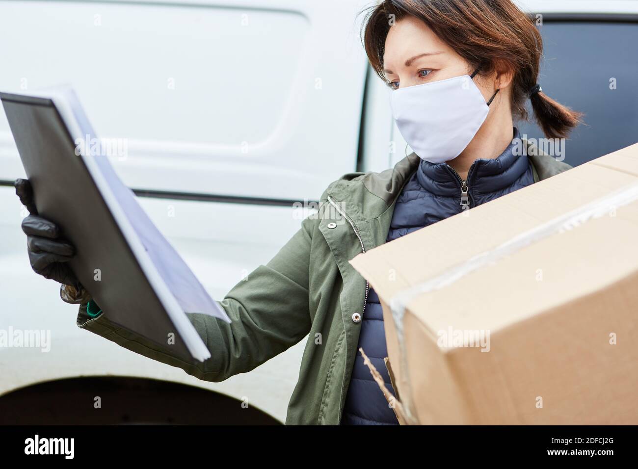 Gestore pacchi di un servizio di consegna con controlli maschera facciale consegna del pacco con lista esterna Foto Stock