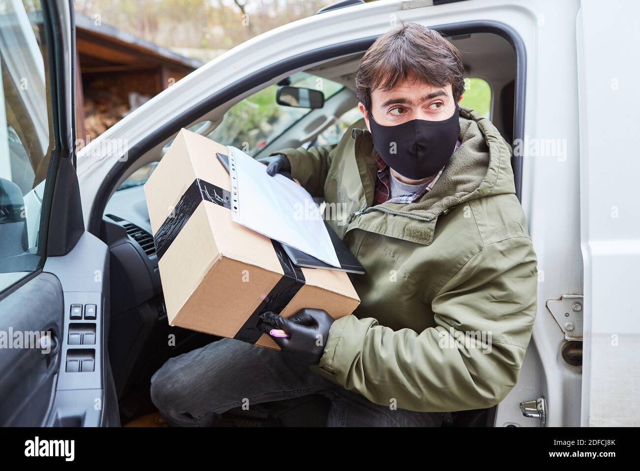 Servizio di consegna pacchi consegna uomo con maschera viso lascia il suo veicolo per la consegna Foto Stock