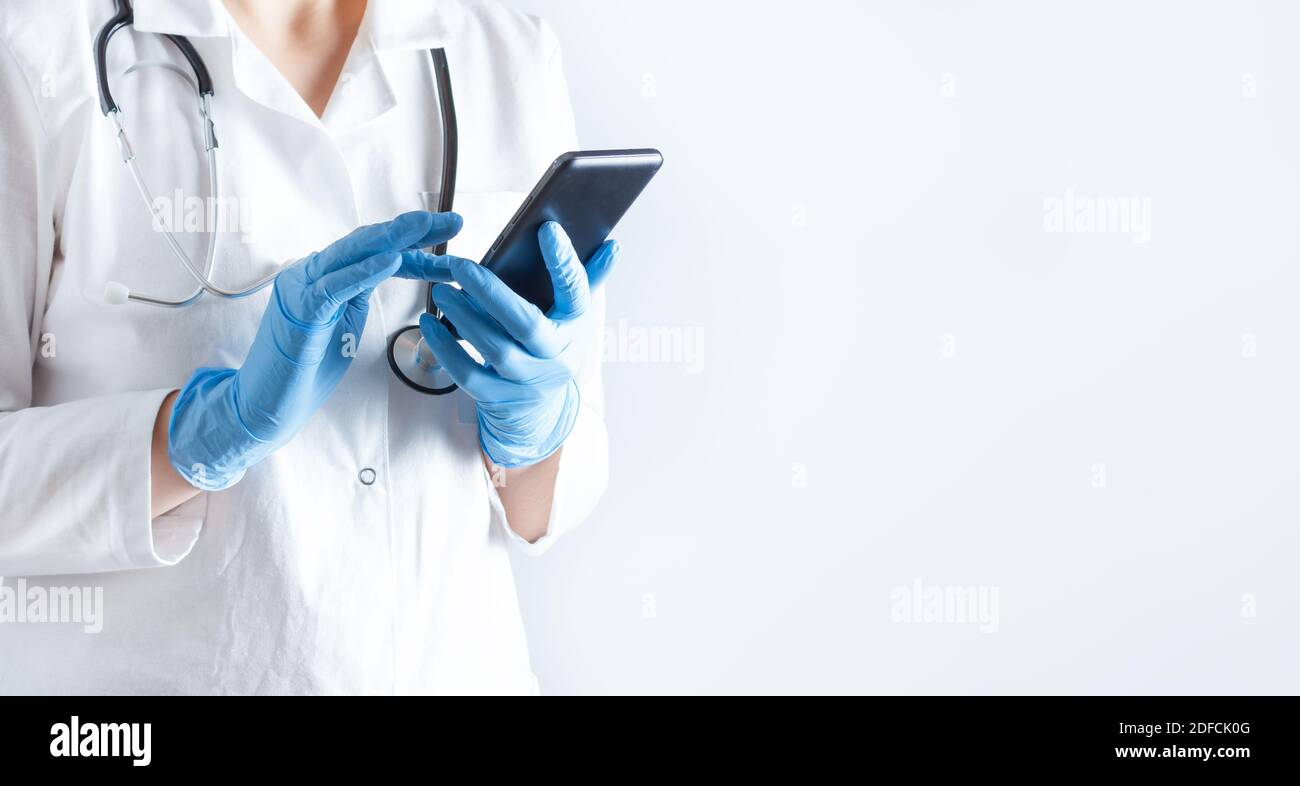 Medico in un camice da laboratorio con telefono cellulare in mani su sfondo bianco. Concetto sanitario e medico. Foto Stock