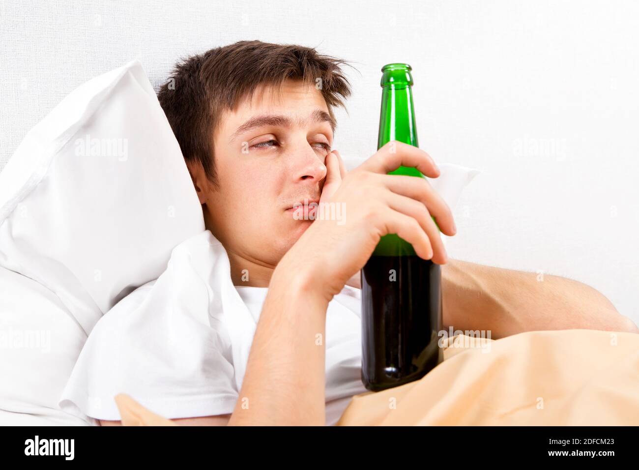 Sleepy giovane uomo con una bottiglia di birra nel letto A casa Foto Stock
