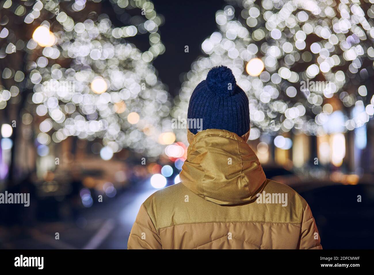Vacanze di Natale in città. Vista posteriore di giovane uomo contro strada illuminata con negozi. Praga, Repubblica Ceca. Foto Stock