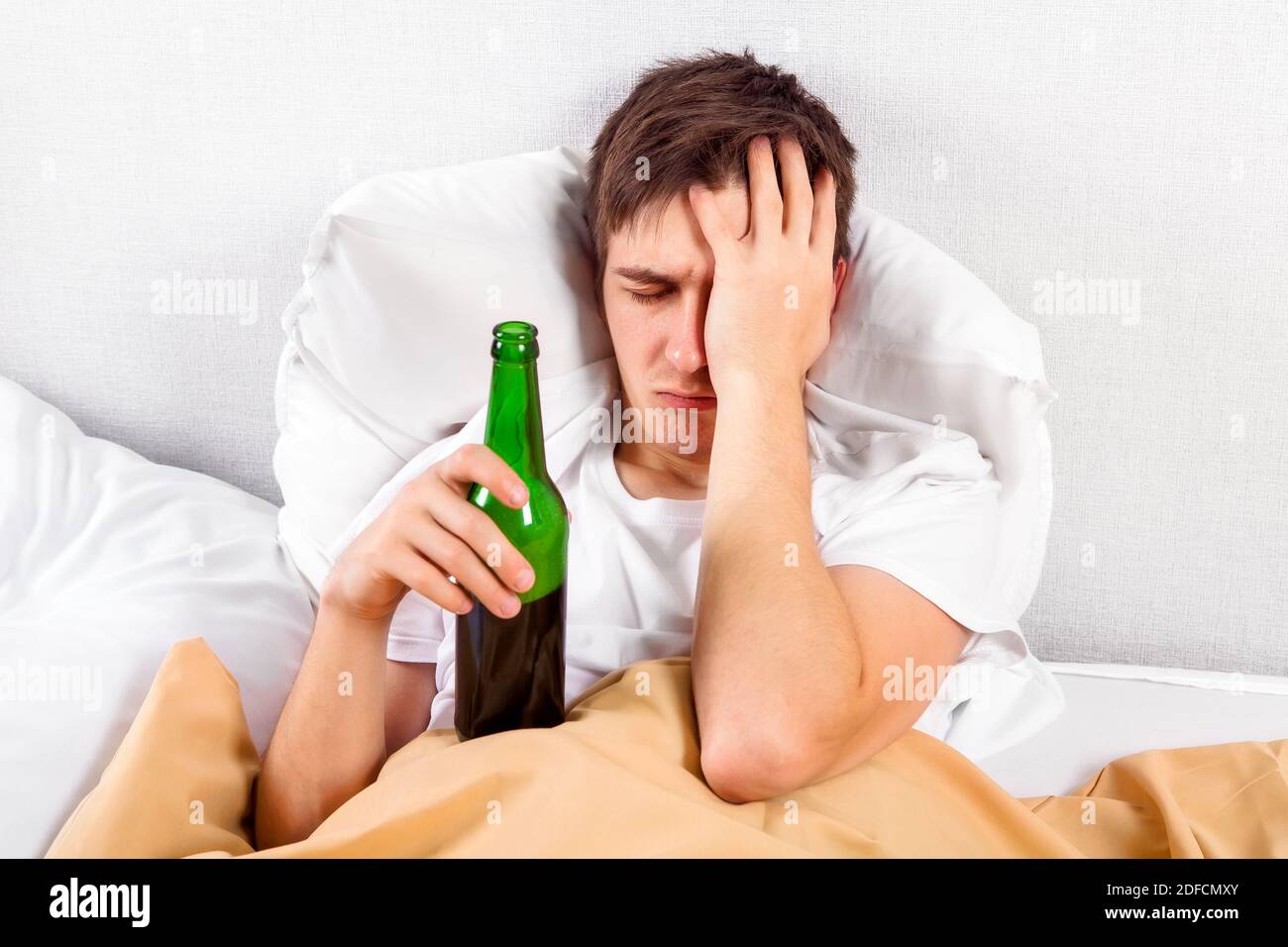 Uomo giovane triste con una bottiglia di birra nel letto A casa Foto Stock