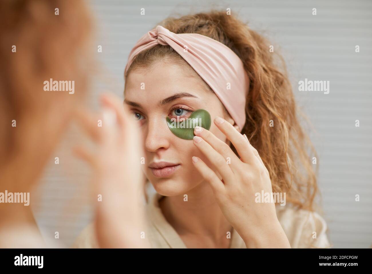 Giovane donna che si prende cura della sua faccia applicando le macchie sotto i suoi occhi guardando lo specchio Foto Stock