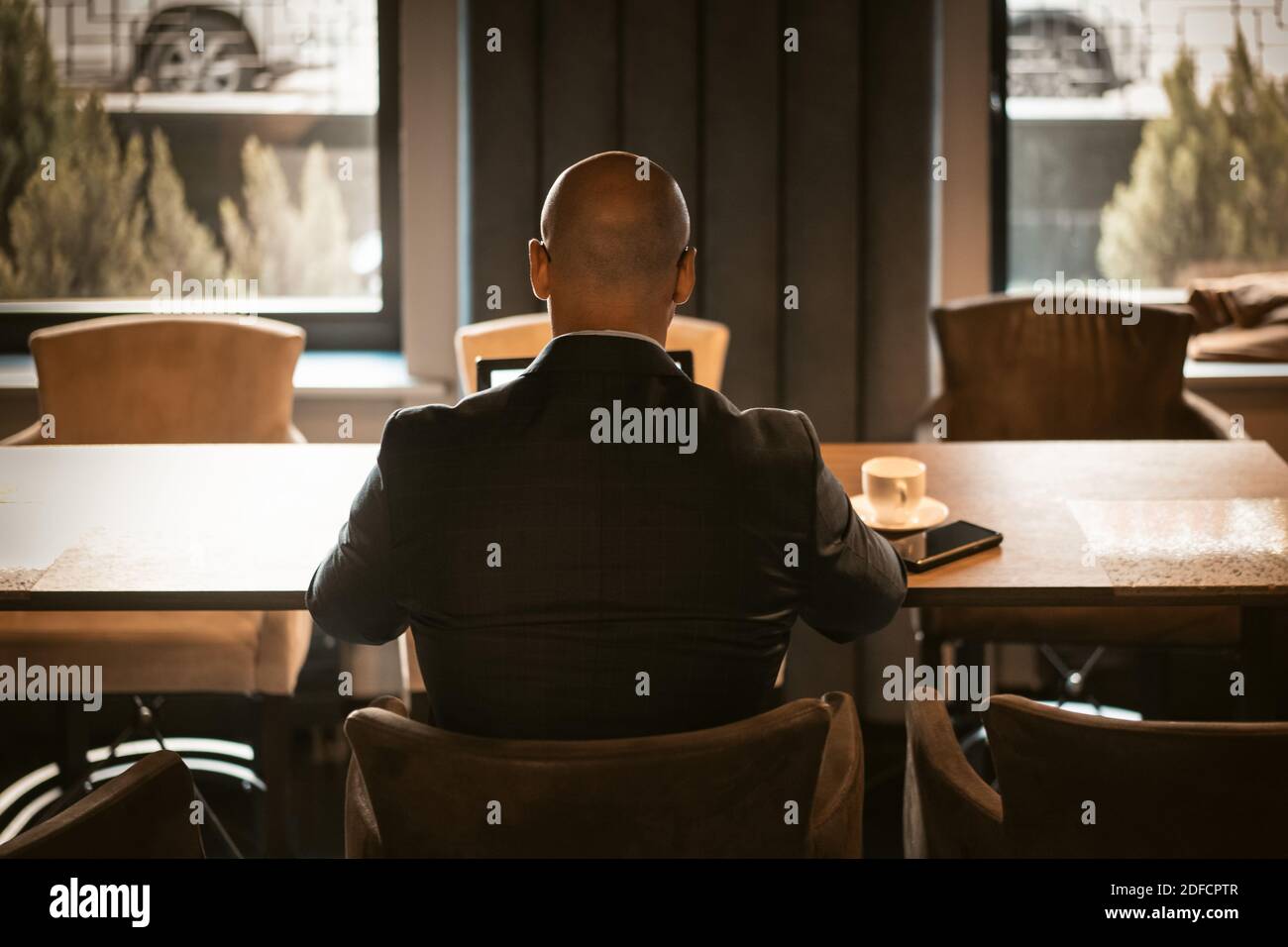 Vista posteriore di un elegante CEO vestito in costume costoso seduto al tavolo nel moderno e costoso ufficio interno, maschio calvo che lavora su computer portatile. Indietro Foto Stock