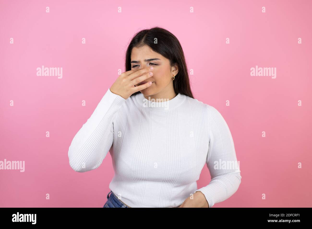 Giovane bella donna su sfondo rosa isolato odore qualcosa di stinoso e disgustoso, odore intollerabile, respiro con le dita sul naso Foto Stock