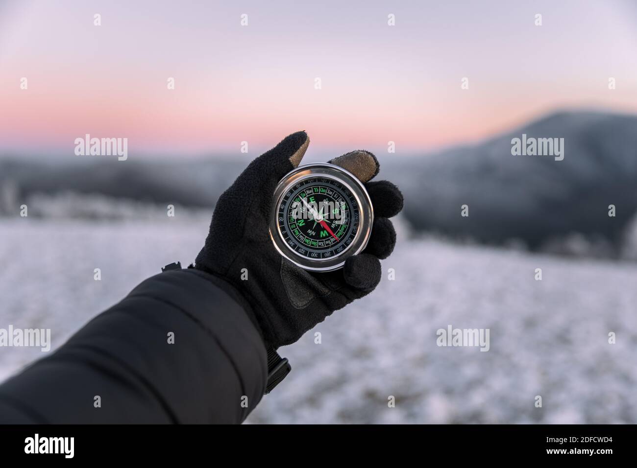 Man explorer ricerca direzione con bussola nella foresta selvaggia invernale al tramonto. Concetto di sopravvivenza Foto Stock