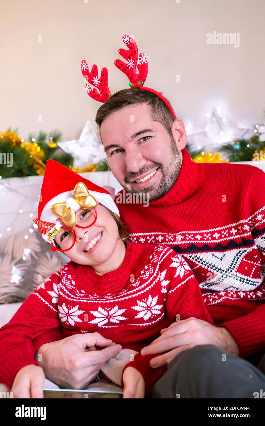 Piccola figlia in cappello di Santa con papà in una stanza decorata per Natale. Buona famiglia che festeggia le vacanze invernali. Foto di alta qualità Foto Stock