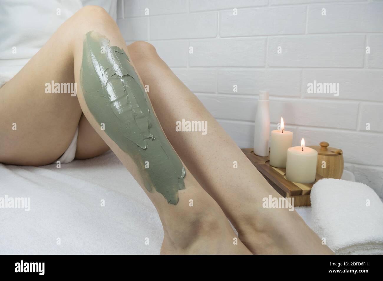 Una donna applica una maschera di argilla alla pelle delle gambe. Peli incarniti. Irritazioni dopo la depilazione e la rasatura. Cura della pelle domestica, corpo. CENTRO BENESSERE, idratante, tre Foto Stock