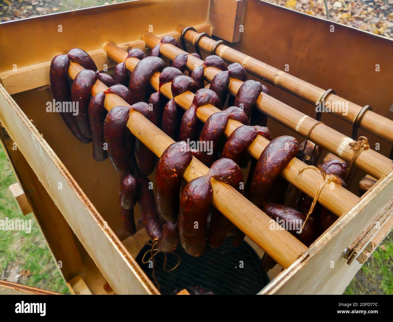 Salsicce fatte in casa appese in legno fumatore all'aperto Foto Stock