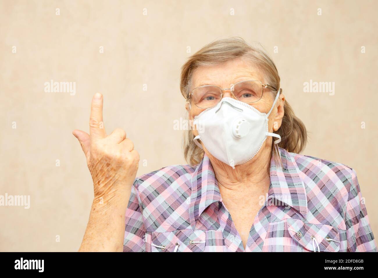 La donna anziana in maschera protettiva punta alla parte superiore della cornice con spazio di testo vuoto, spazio di copia Foto Stock