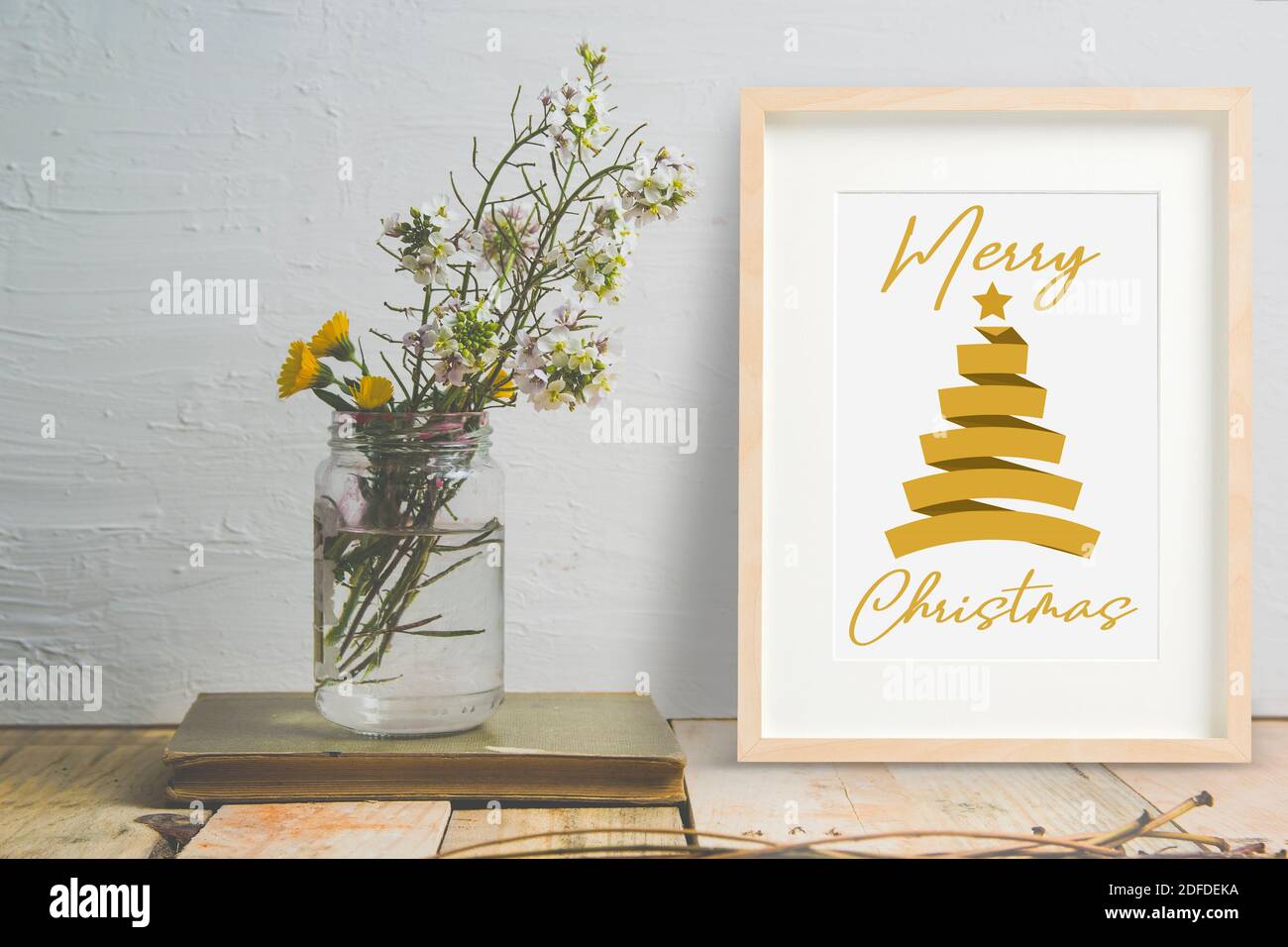 Allegro biglietto di auguri di Natale in una cornice accanto a un vaso con alcuni fiori e spazio di copia vuoto per il testo del redattore. Foto Stock