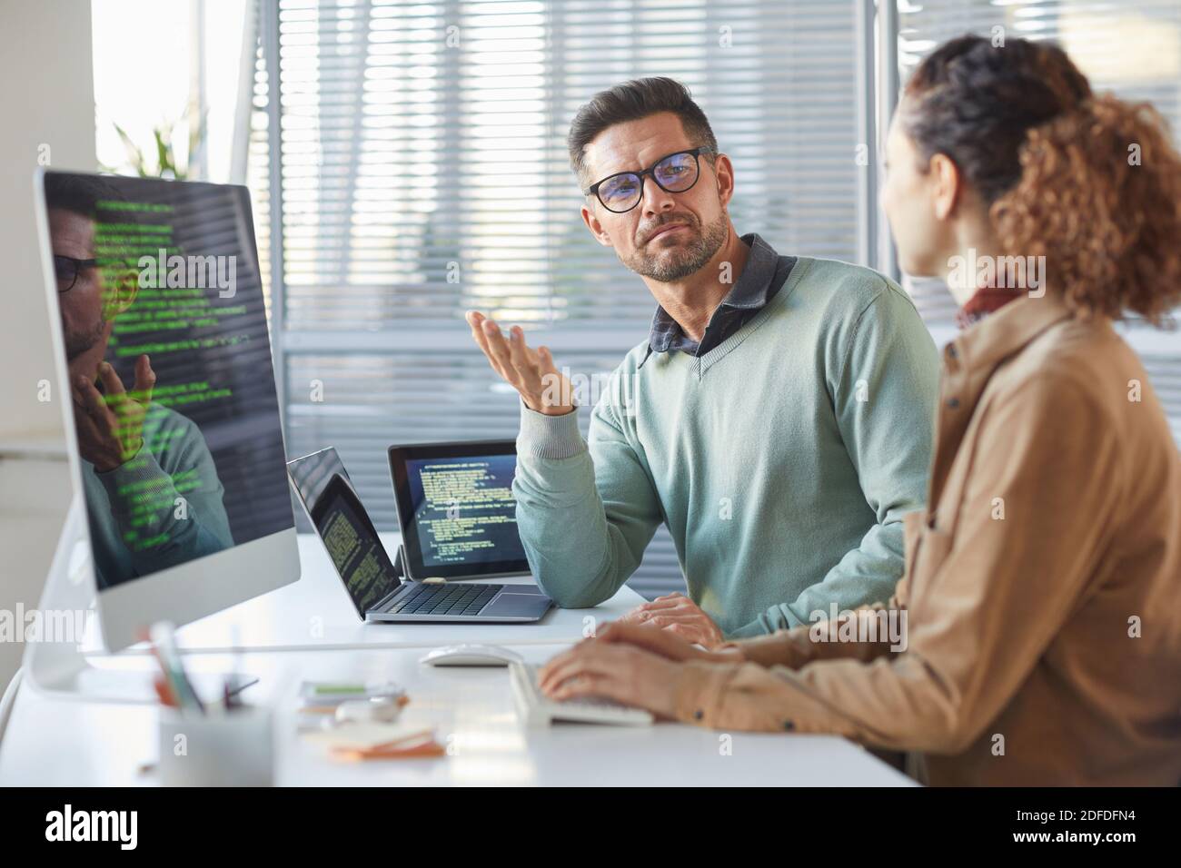 Due colleghi seduti al tavolo davanti ai computer E discutere del nuovo software nell'ufficio IT Foto Stock