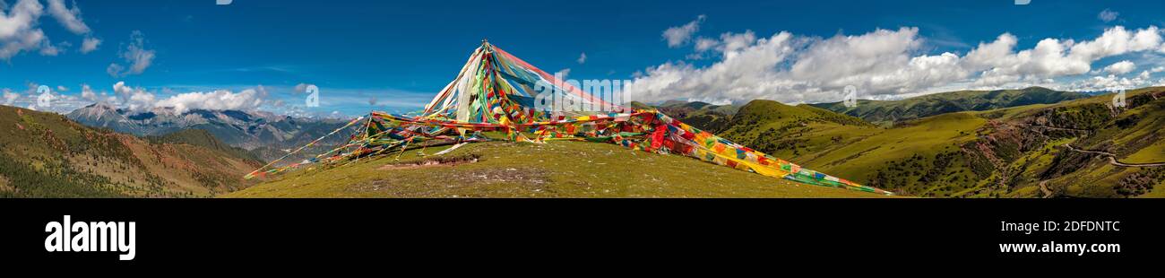 Panorama molto ampio delle bandiere di preghiera tibetane in un palo in cima a una montagna rotonda in una natura incontaminata con solo una strada sterrata visibile sul ri Foto Stock