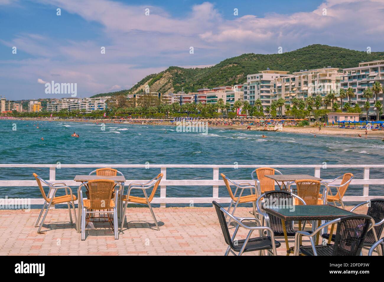 Valona/Albania - 7 agosto 2020: Stazione estiva – caffè all'aperto – tavoli e sedie, acqua di mare turchese, persone che nuotano, solarium sulla spiaggia, hotel Foto Stock