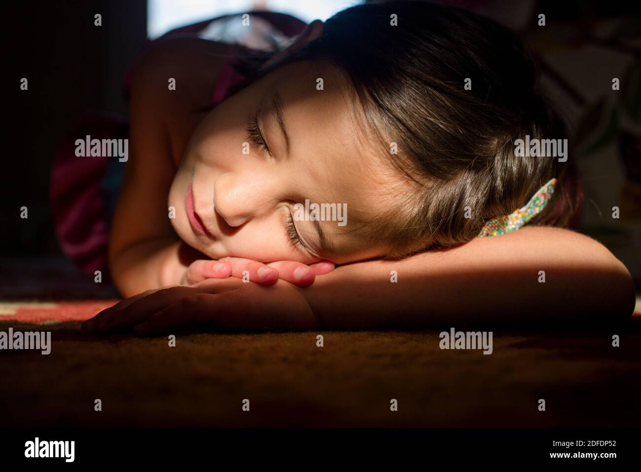 Una bambina si stende in un luminoso punto di luce con occhi chiusi sorridenti Foto Stock