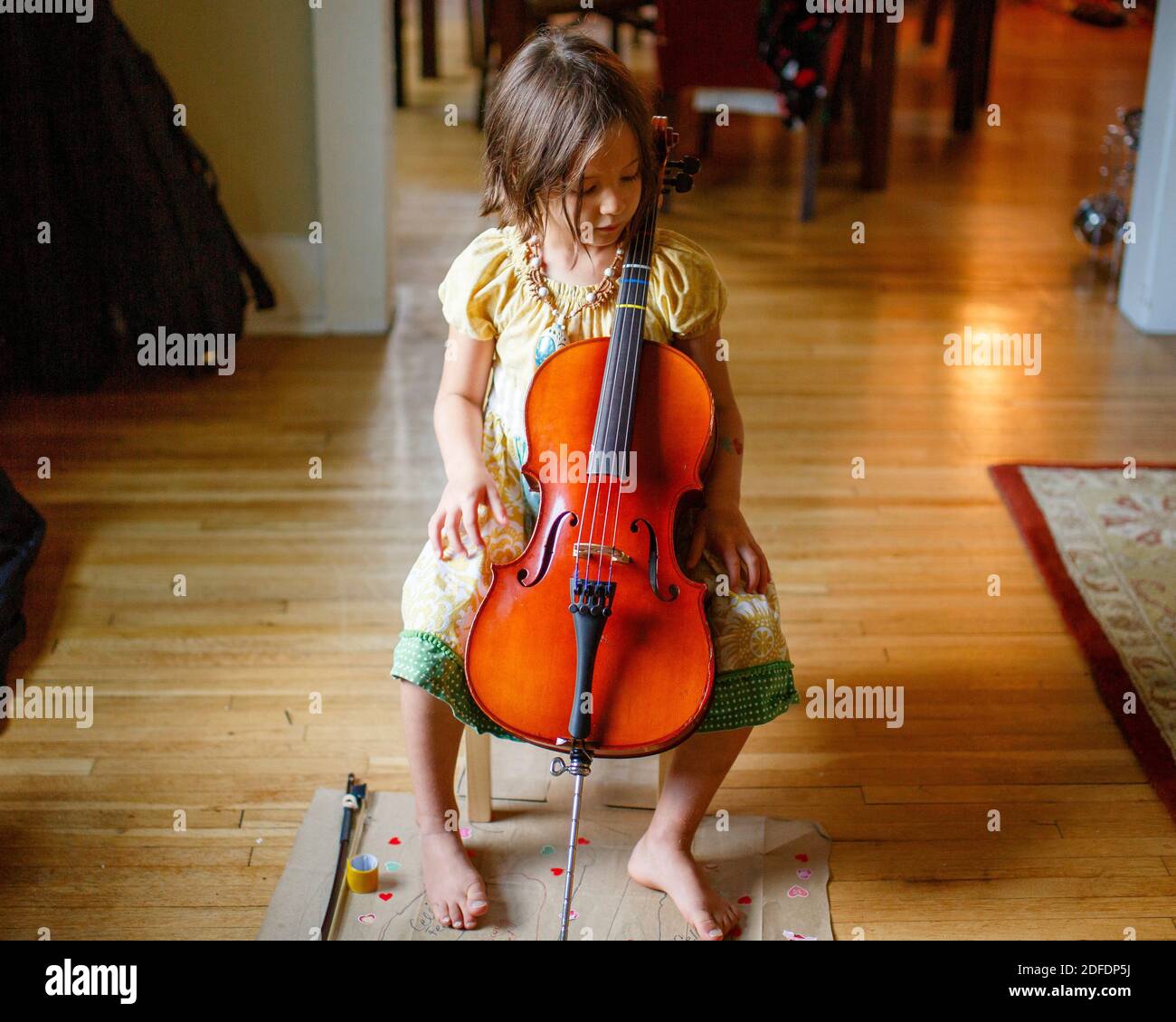 sopra-vista del bambino a piedi nudi carino nella luce della finestra che tiene un piccolo violoncello Foto Stock