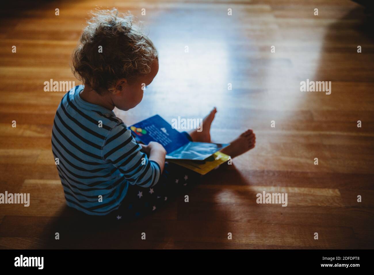 Bambino seduto a terra che legge un libro durante isolamento Foto Stock