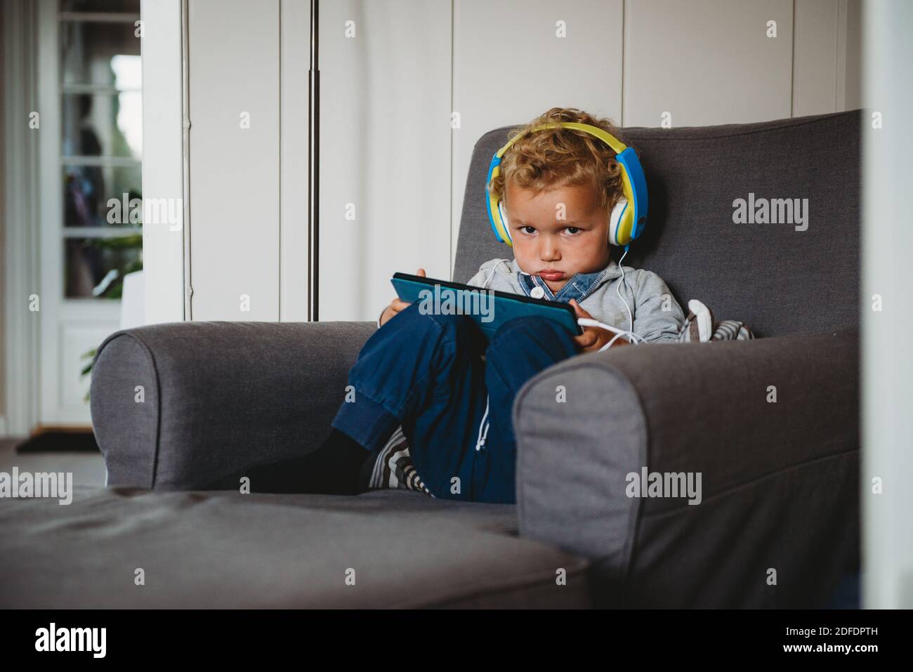 Ragazzo che inpouisce giocando con un tablet e indossando le cuffie a. casa covid Foto Stock