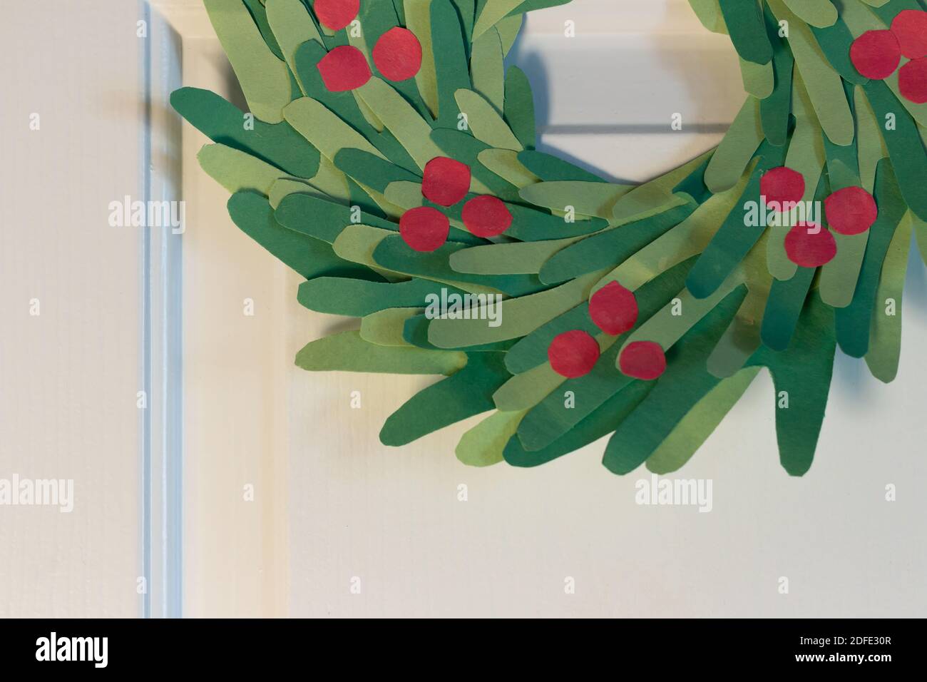 Corona di Natale fatta in casa per i bambini sulla porta bianca con spazio copia, sfondo stagionale Foto Stock