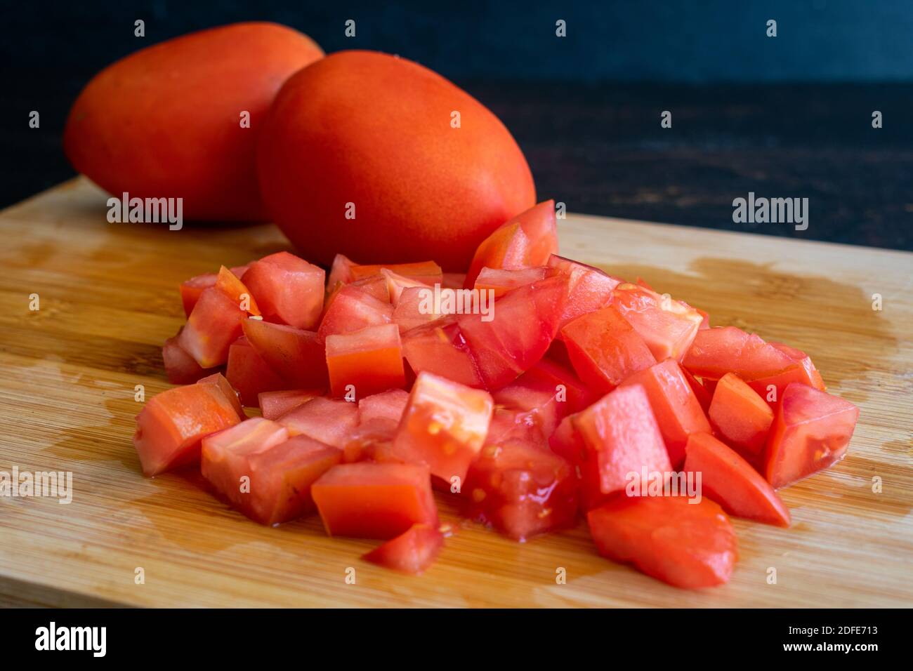 Tagliare i pomodori Roma: Tritare i pomodori freschi. Su un tagliere di bambù Foto Stock