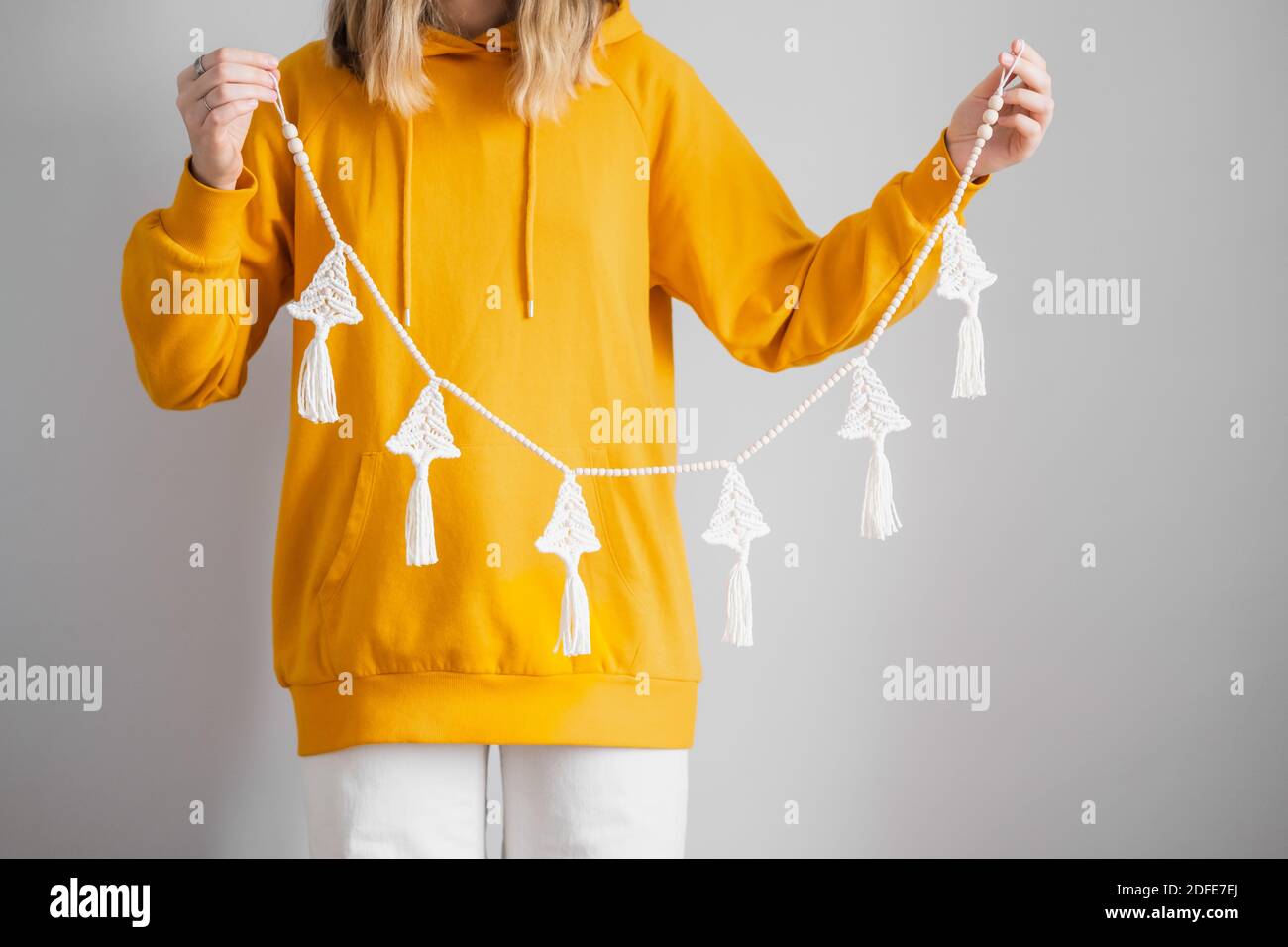 Crochet artigianale nuovo anno decorazione in mani donna. Persona in felpa con cappuccio gialla tiene una ghirlanda di natale. Decorazione casa per concetto di vacanze invernali Foto Stock