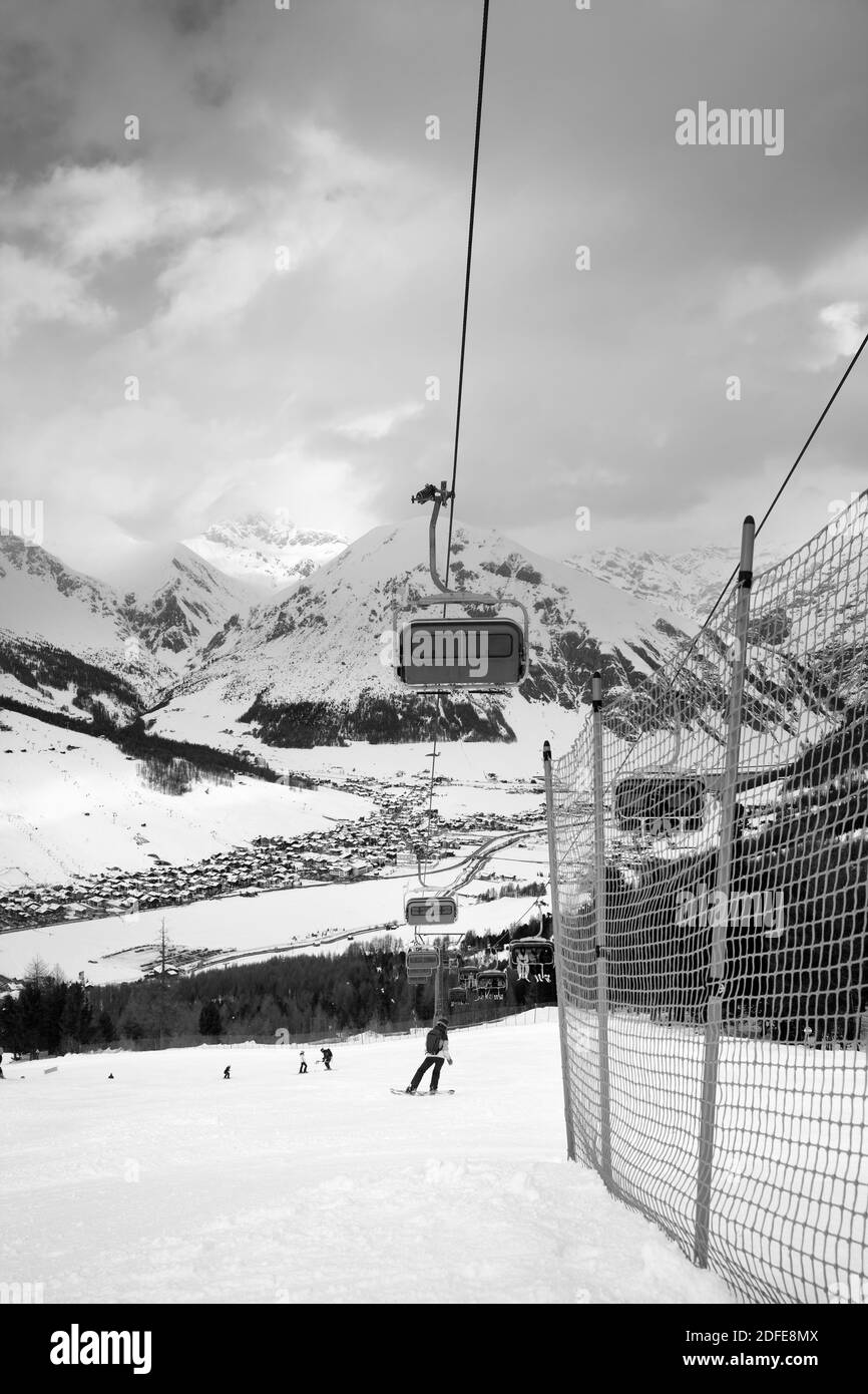 Seggiovia, pista da sci innevata con snowboarder e sciatori in alta montagna e cielo nuvoloso illuminato in inverno. Comprensorio sciistico Mottolino, Alpi Italiane. Livigno L Foto Stock