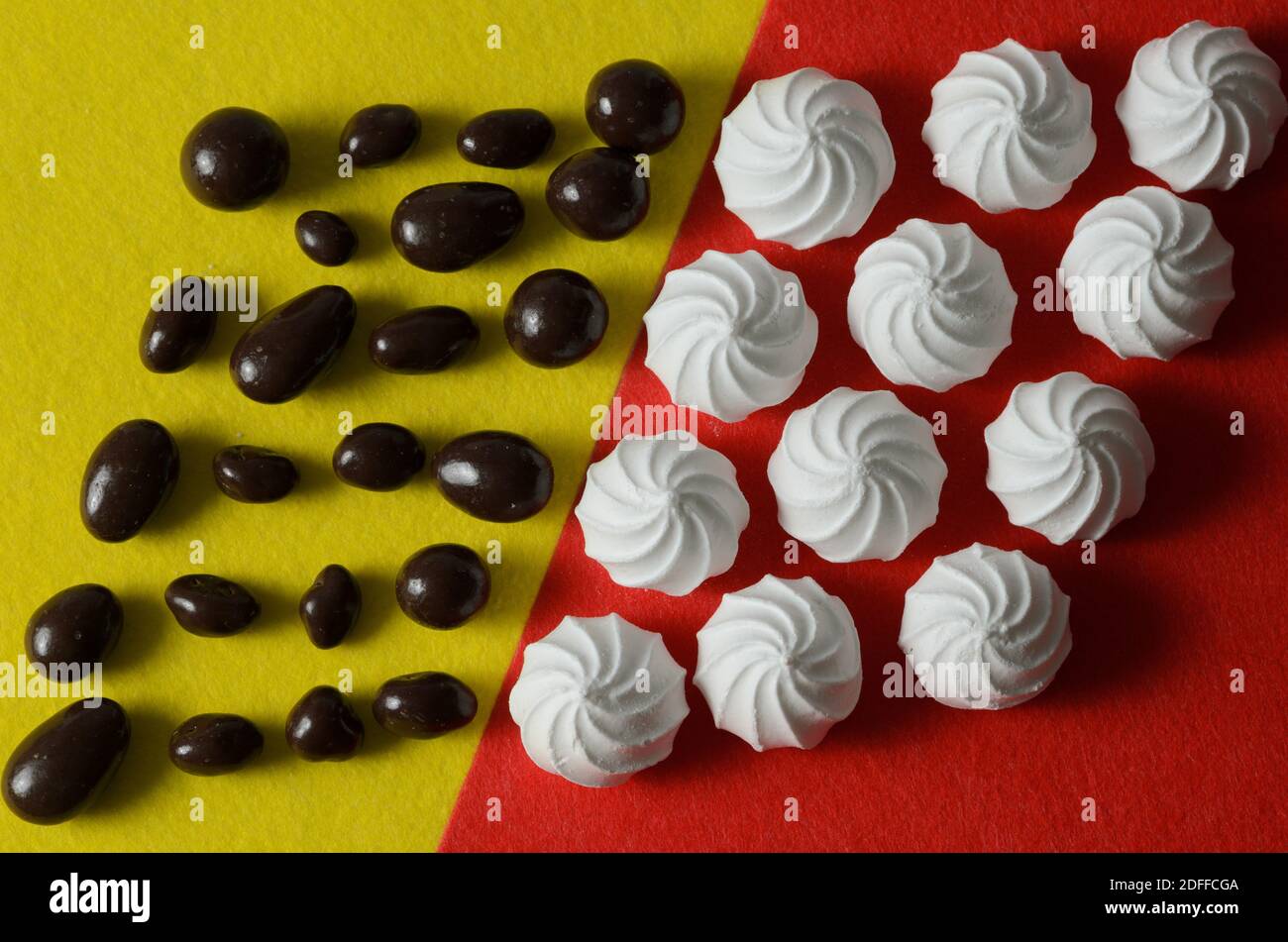 Meringa bianca su sfondo rosso con caramelle tonde al cioccolato su sfondo giallo. Messa a fuoco selettiva. Foto Stock