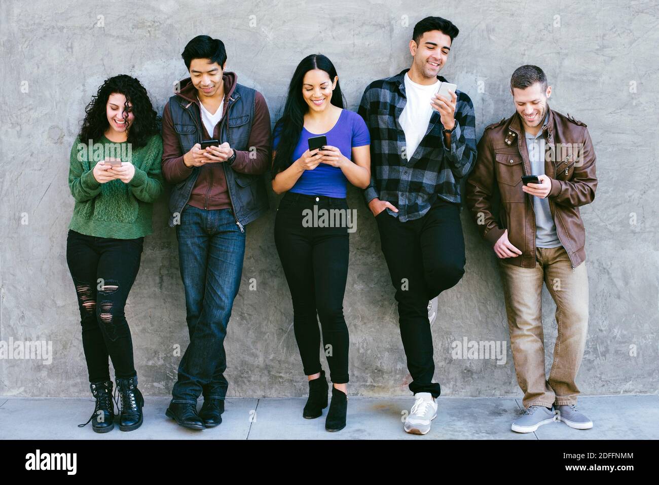 Amici che si levano in piedi l'uno accanto all'altro e che stanno fissando loro Telefoni cellulari - Nessuna comunicazione - SMS - Giochi Foto Stock